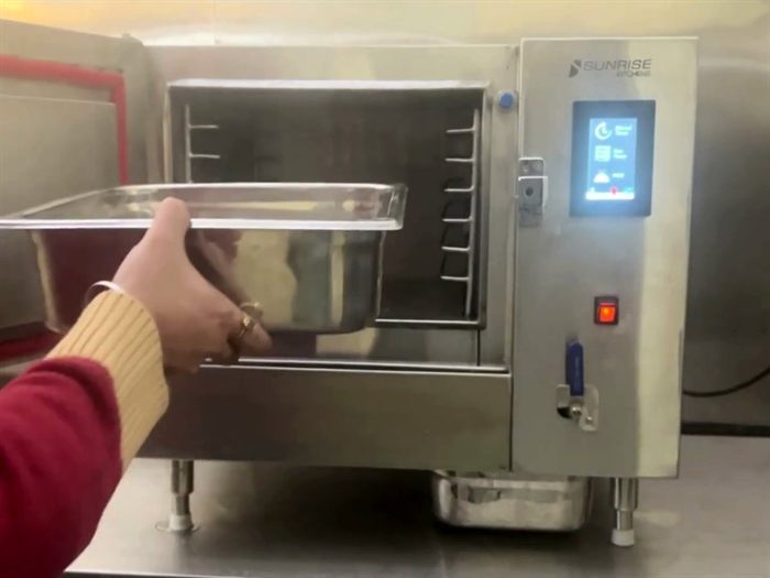 Loading a GN 1/1 stainless steel pan into the Cook and Hold Steamer cavity, with the touchscreen control panel beside it
